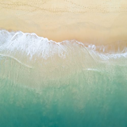 Aerial view of turquoise ocean wave reaching the coastline. Beautiful tropical beach from top view. Andaman sea in Thailand. Summer holiday vacation concept